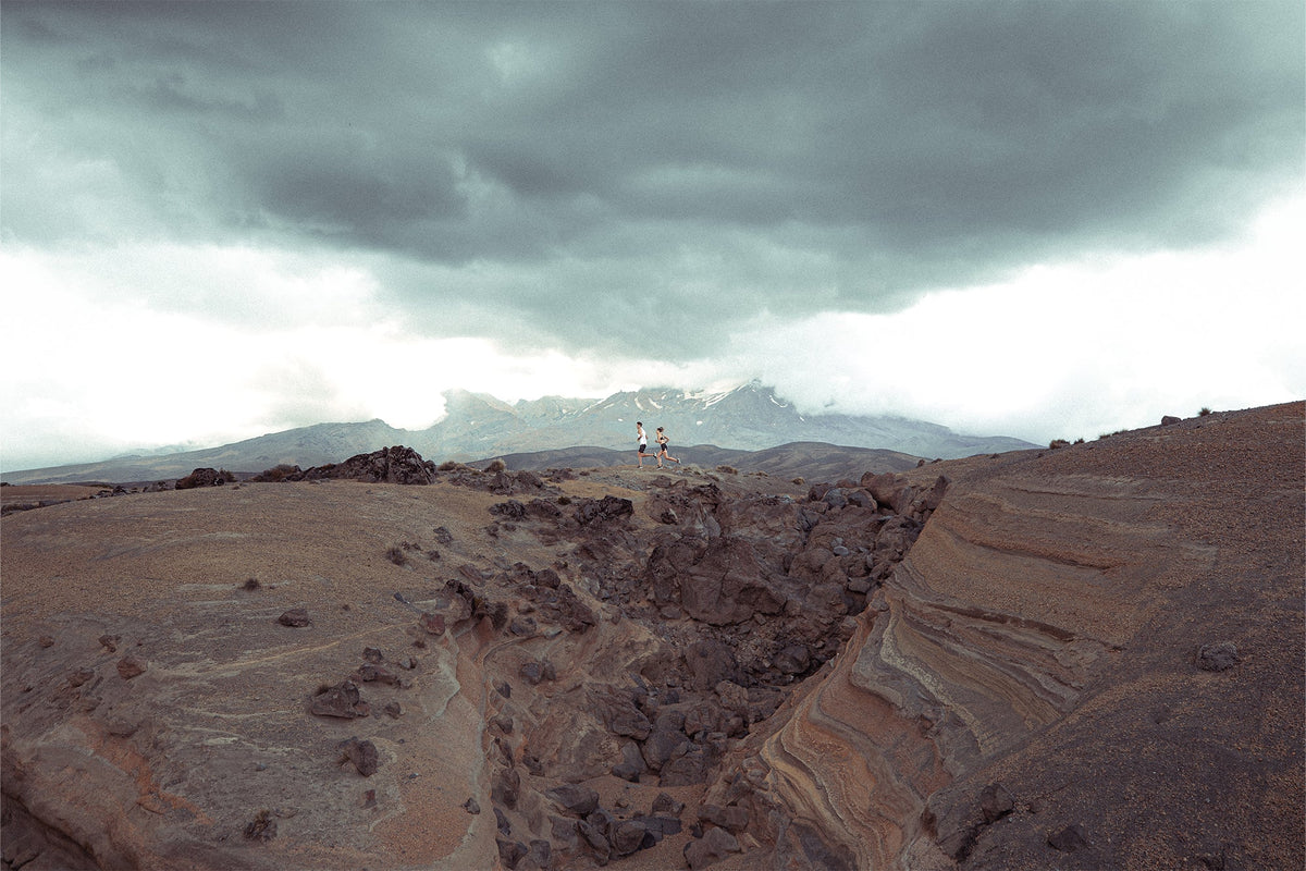 Runners crossing a rugged, rocky landscape under stormy skies
