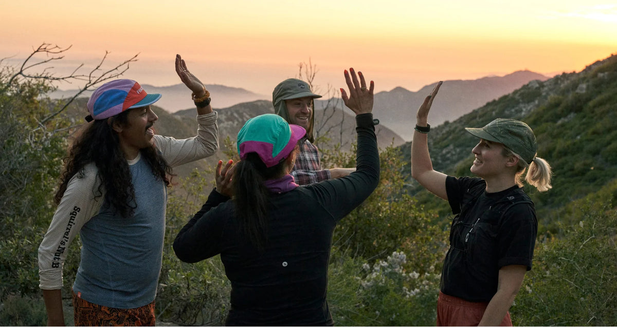 Group of trail runners in Fractel caps celebrating together on a hillside at sunset
