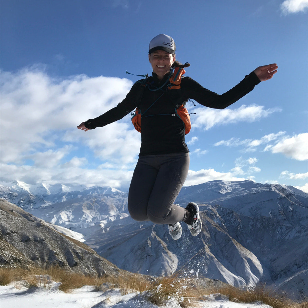 Jane on top of a snowy mountain jumping up into the air.