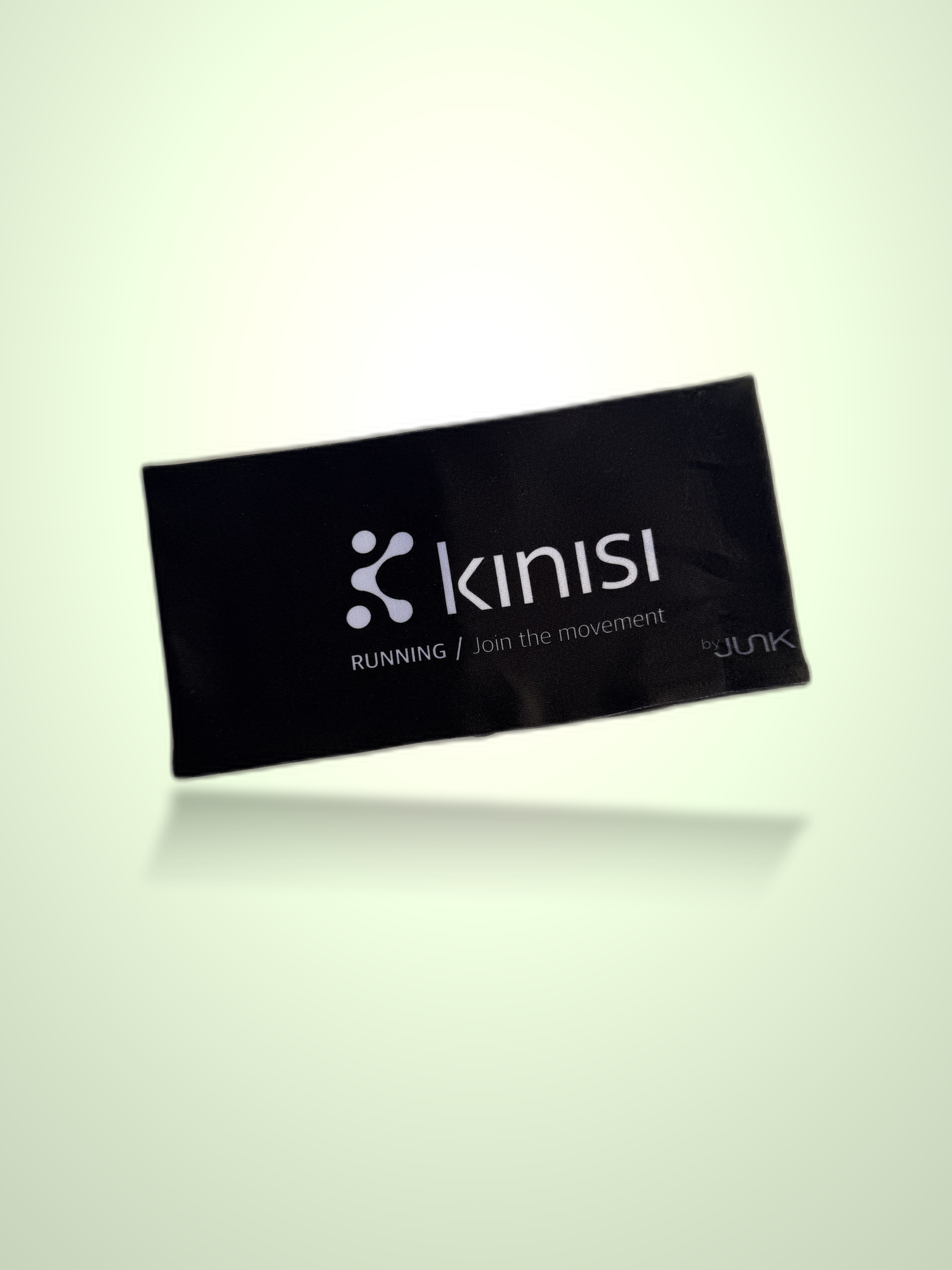 A black athletic headband with white Kinisi branding and text, shown floating against a pale green gradient background with a soft reflection below.