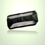 A dark olive green fabric headband with a white inner lining, shown floating against a light green gradient background with a soft reflection underneath.