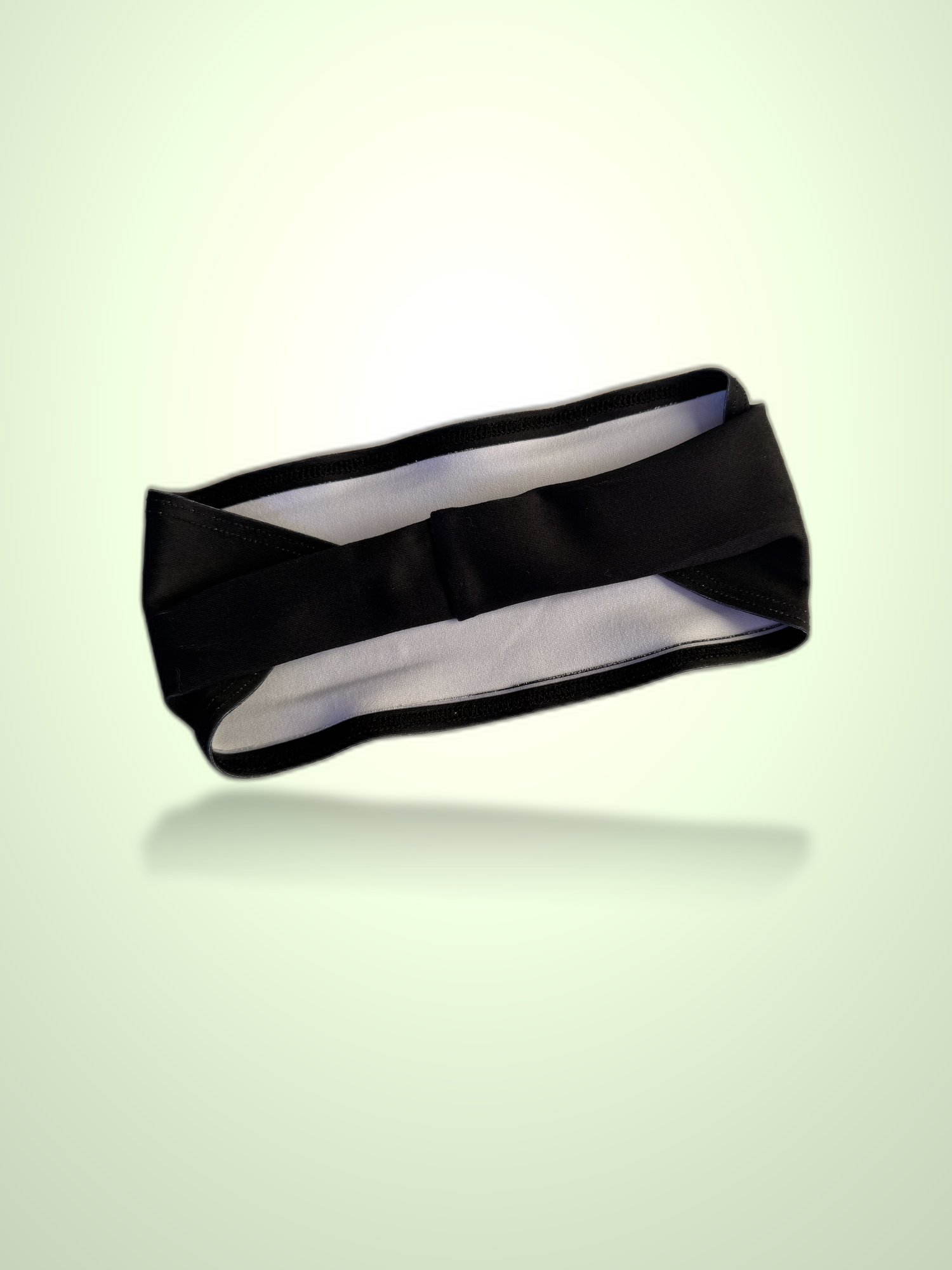 A black athletic headband with a white inner lining, shown floating against a light green gradient background with a soft reflection underneath.