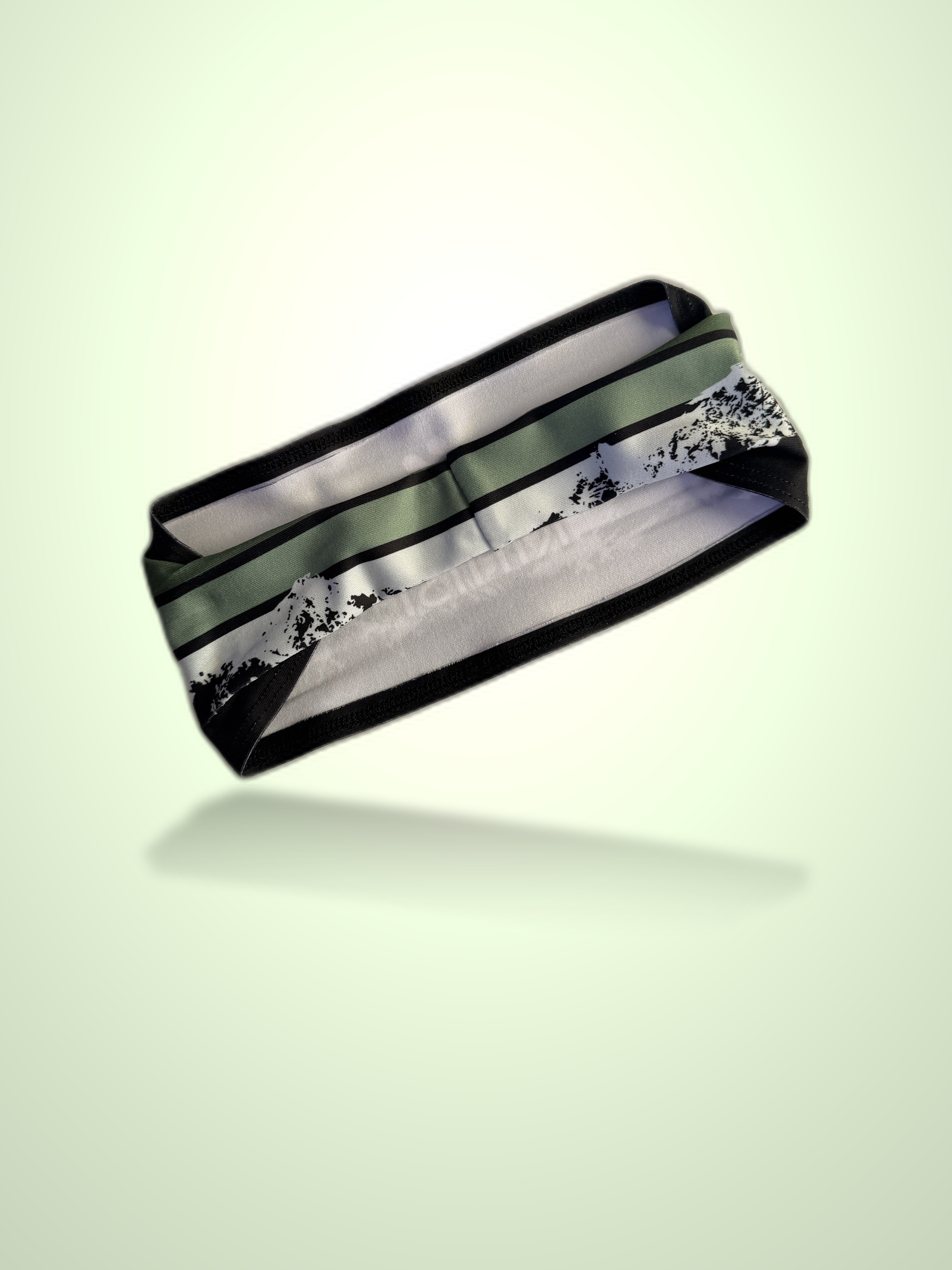 A black athletic headband with a green stripe and a white mountain pattern, shown floating against a pale green background.