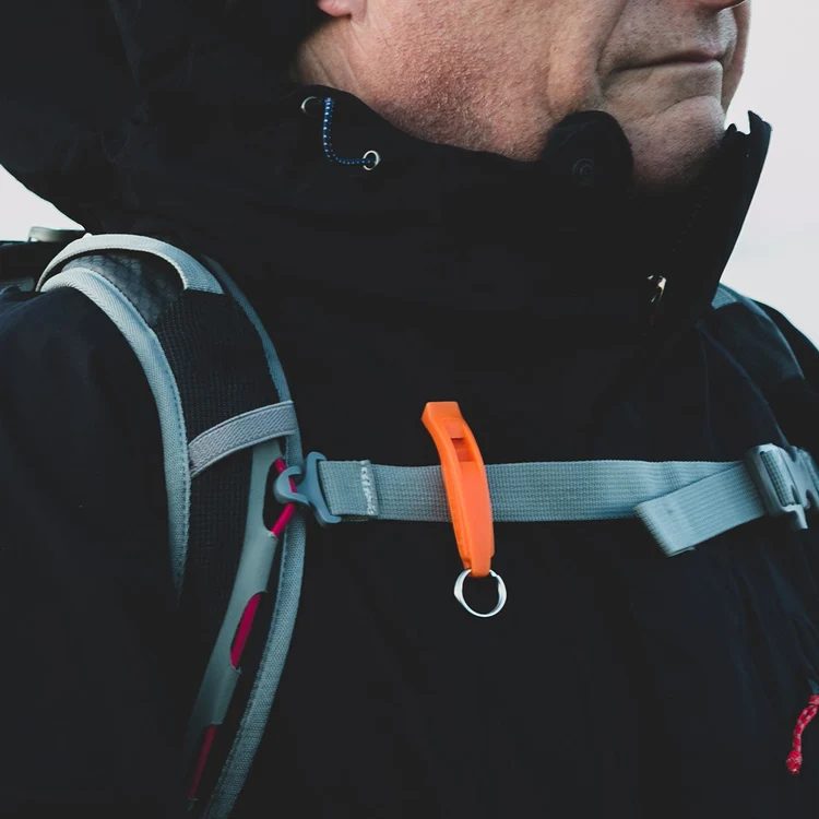 Close-up of a person wearing a black jacket and backpack, with an orange whistle clipped to the chest strap.