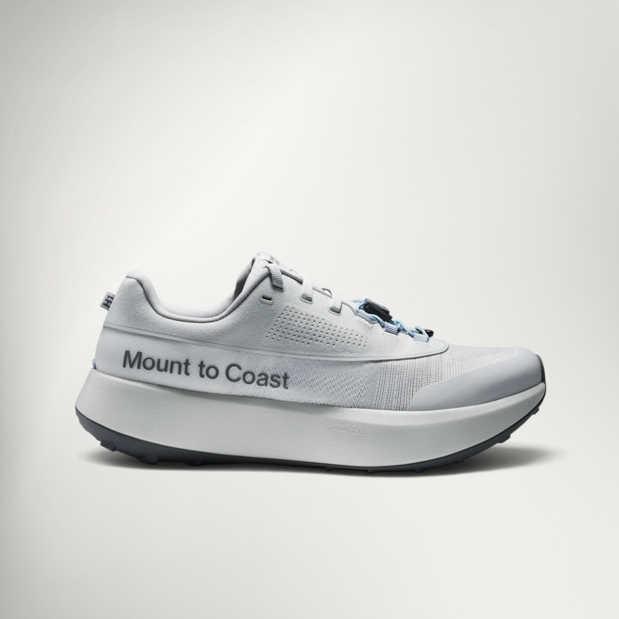 A light gray and white Mount to Coast running shoe shown from the side against a clean, light gray studio background.