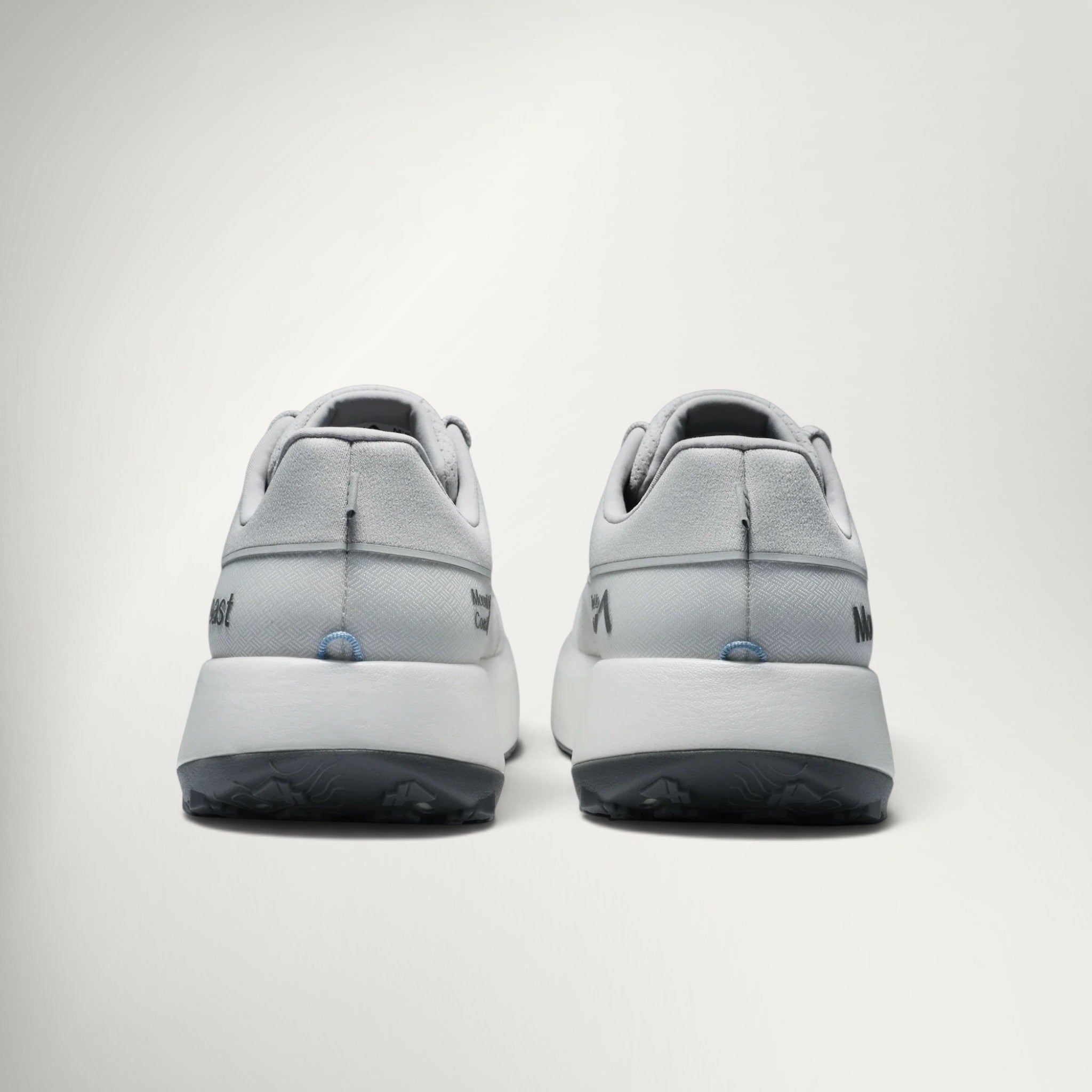 A pair of light gray athletic sneakers shown from the back, featuring thick white midsoles and dark gray outsoles, set against a clean off-white background.