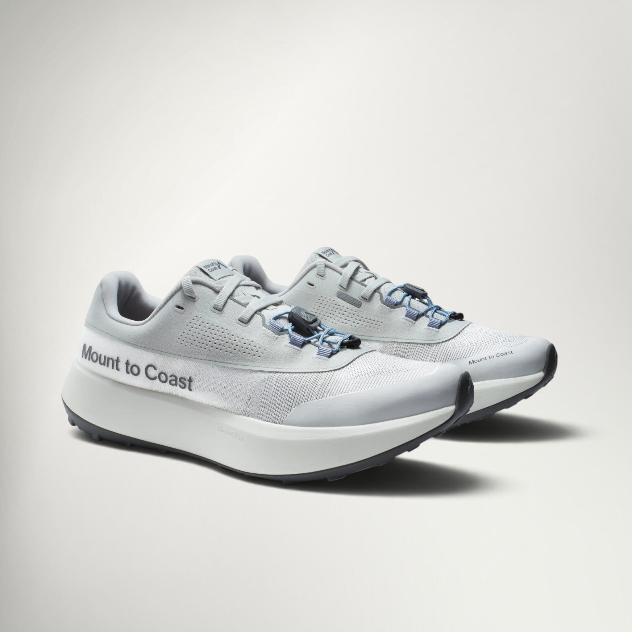 A pair of Mount to Coast athletic sneakers in light gray and white with blue accents on the laces, displayed on a clean light gray background.