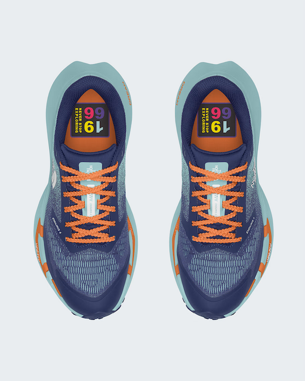 A pair of The North Face running shoes shown from a top-down view on a light gray background. The shoes feature a navy blue mesh upper with bright orange laces, orange accents on the midsole, and a light teal/blue-green outer sole.