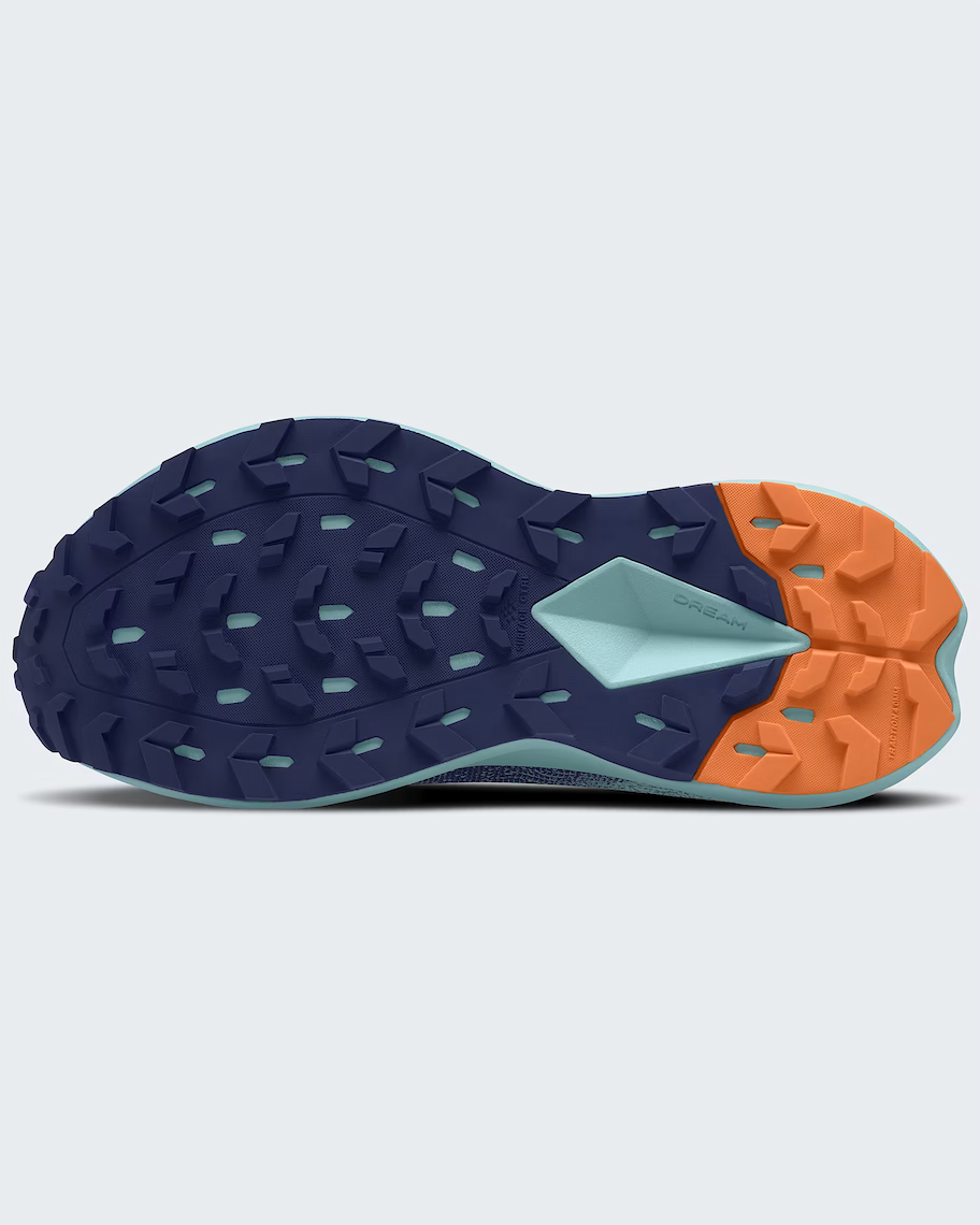 The outsole of a The North Face trail running shoe shown from a top-down view, featuring a dark navy blue tread with a light blue geometric accent and a bright orange rear section.
