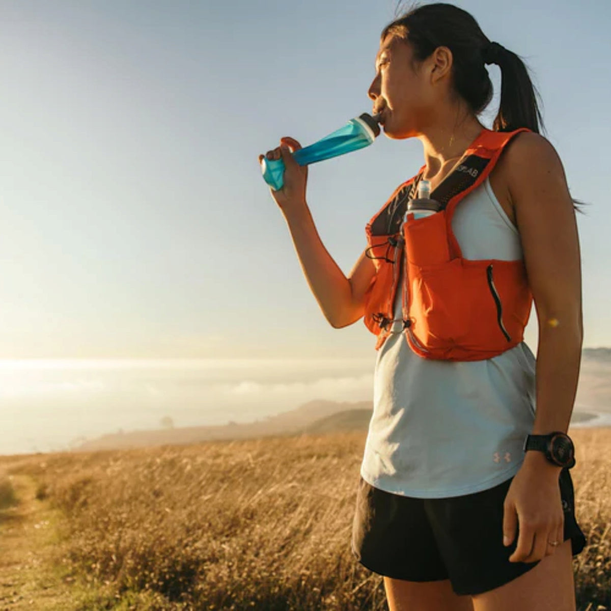 Trail runner in a HydraPak vest drinking from a soft flask in golden grassland