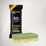 A Precision Fuel chew bar package in black with white text and a small rainbow accent, shown next to a mint-green and pale yellow chew bar on a light gray background.
