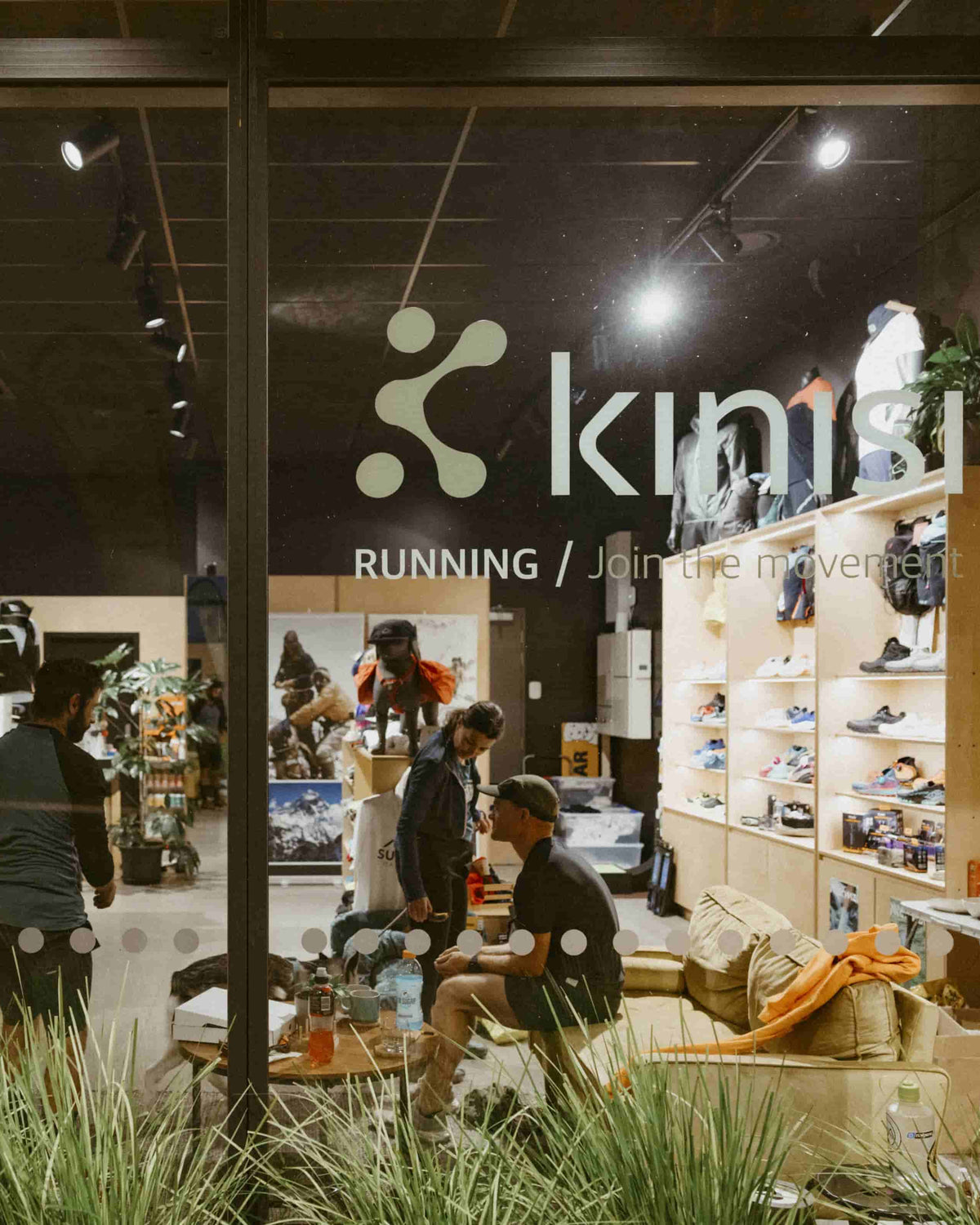 Looking through the Kinisi Running shop window at night, with people inside hanging out and chatting