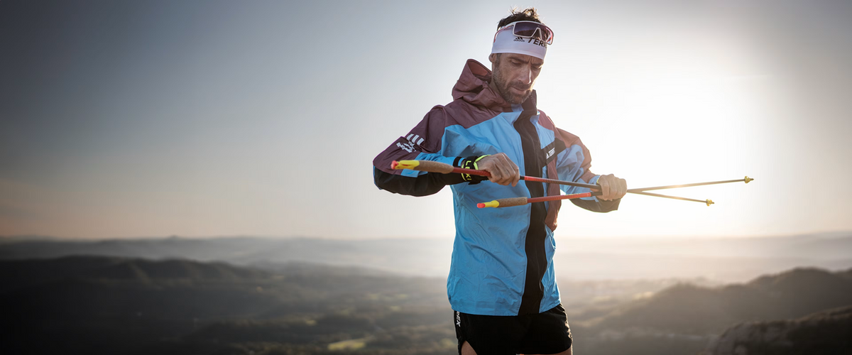 Trail runner holding Leki poles on a mountain ridge with hazy hills behind