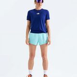 A model stands against a light gray studio background wearing a navy blue short-sleeve athletic t-shirt with a small white chest logo, light aqua running shorts, a matching light aqua visor, reflective sunglasses, white socks, and blue running shoes with orange laces. The t-shirt brand is The North Face.