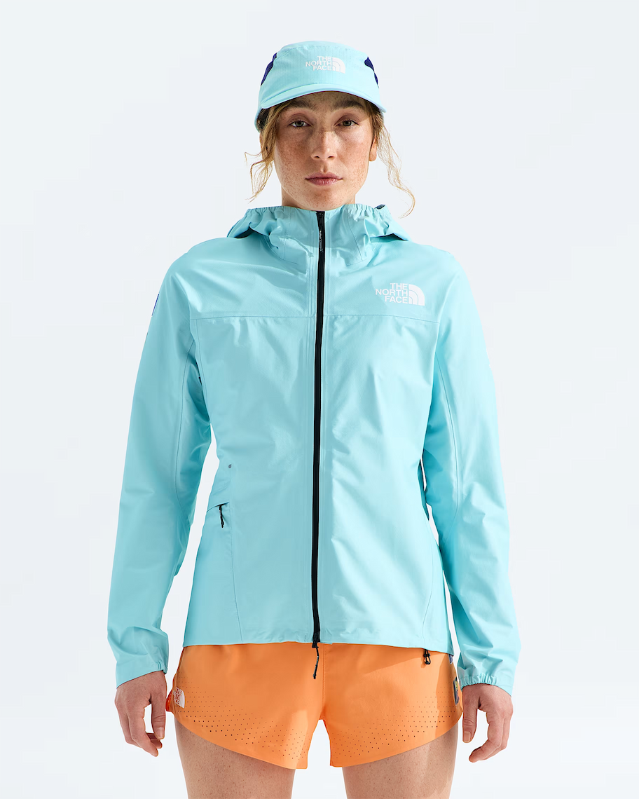 A woman modeling a light blue hooded jacket and matching cap from The North Face, paired with orange shorts, against a clean white studio background.