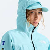A close-up of a woman wearing a light blue hooded jacket and matching cap, with The North Face branding visible on the chest and sleeve.