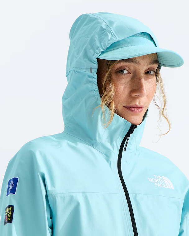A close-up of a woman wearing a light blue hooded jacket and matching cap, with The North Face branding visible on the chest and sleeve.