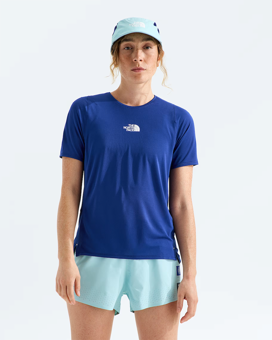 A woman modeling a royal blue short-sleeve athletic t-shirt with a small white The North Face logo on the chest, paired with light blue shorts and a matching light blue cap, against a plain white studio background.