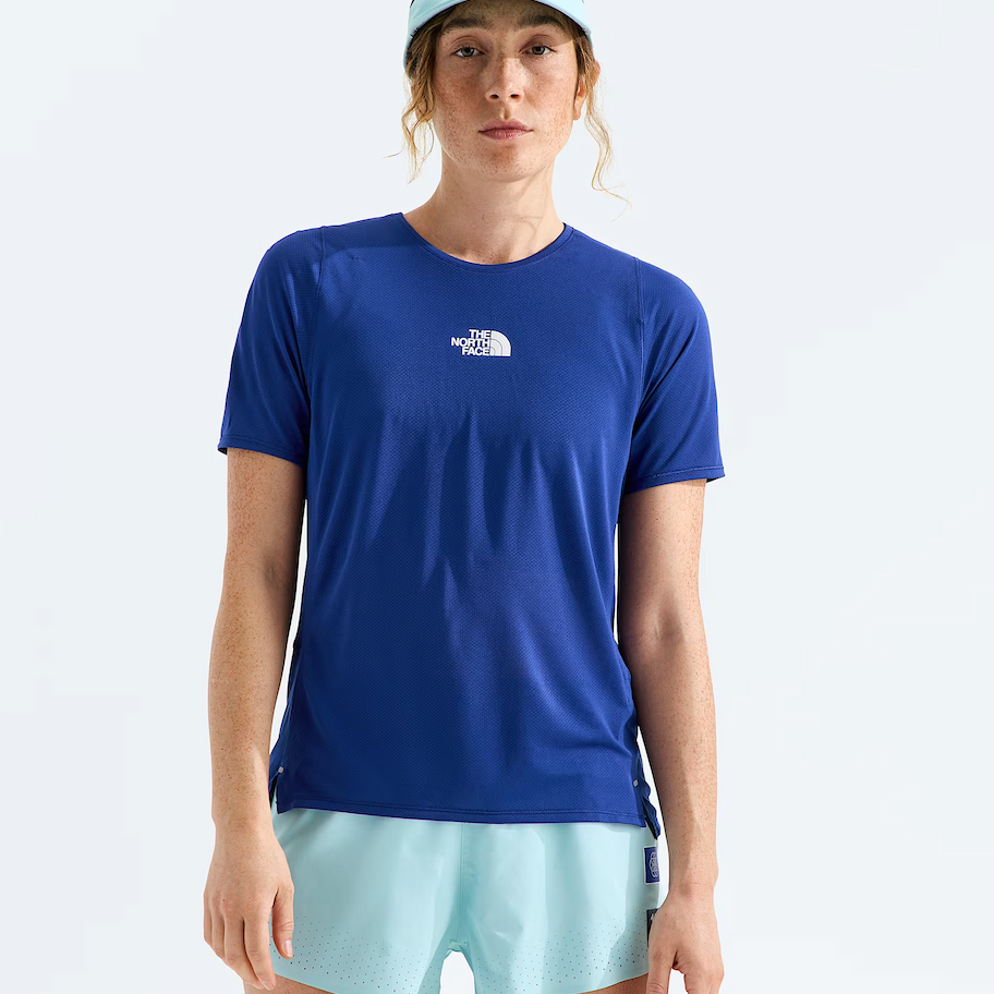 A woman modeling a royal blue short-sleeve athletic t-shirt with a small white The North Face logo on the chest, paired with light blue shorts and a matching light blue cap, against a plain white studio background.