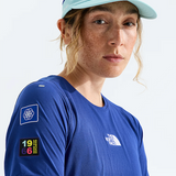 A close-up of a woman wearing a blue The North Face athletic t-shirt and a light blue cap, photographed against a clean white studio background.