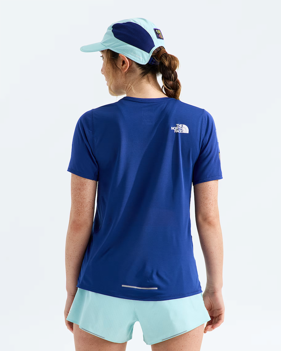 A woman shown from the back wearing a royal blue short-sleeve athletic T-shirt with a small white The North Face logo on the upper back, paired with light mint shorts and a matching two-tone cap, against a clean white studio background.
