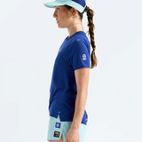 A woman in side profile wearing a royal blue athletic t-shirt, light blue athletic shorts, and a matching light blue visor against a clean white studio background.