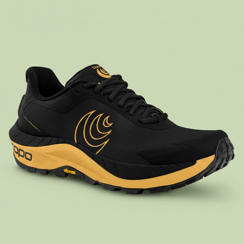 Black and yellow Topo running shoe on a pale green background.