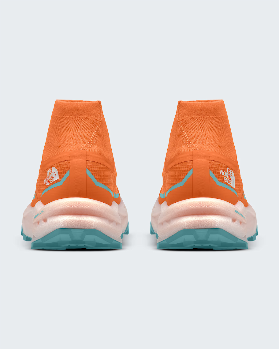 A pair of The North Face sneakers shown from the back, featuring a vibrant orange knit upper, a thick pale pink and white midsole, and teal outsoles.