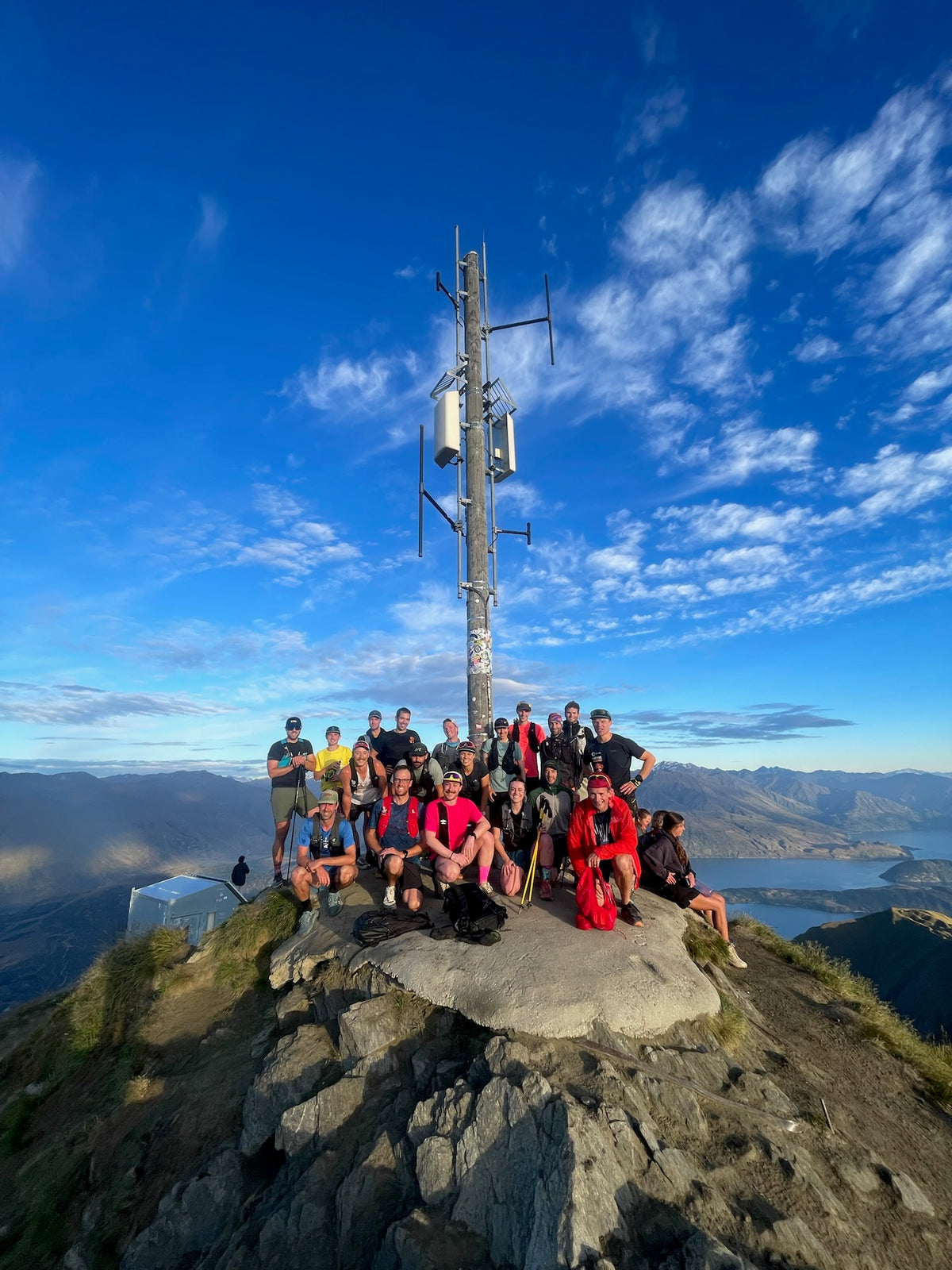 The Kinisi Running Froyday crew gathered at the summit of Roy's Peak under a bright blue sky, with Lake Wānaka below