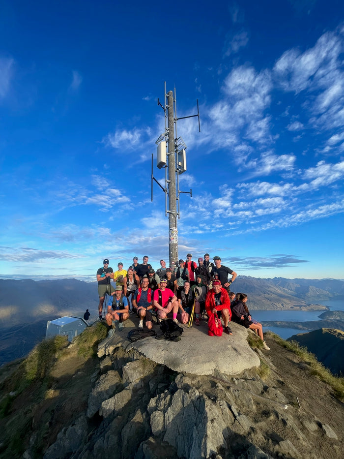 The Kinisi Running Froyday crew gathered at the summit of Roy's Peak under a bright blue sky, with Lake Wānaka below