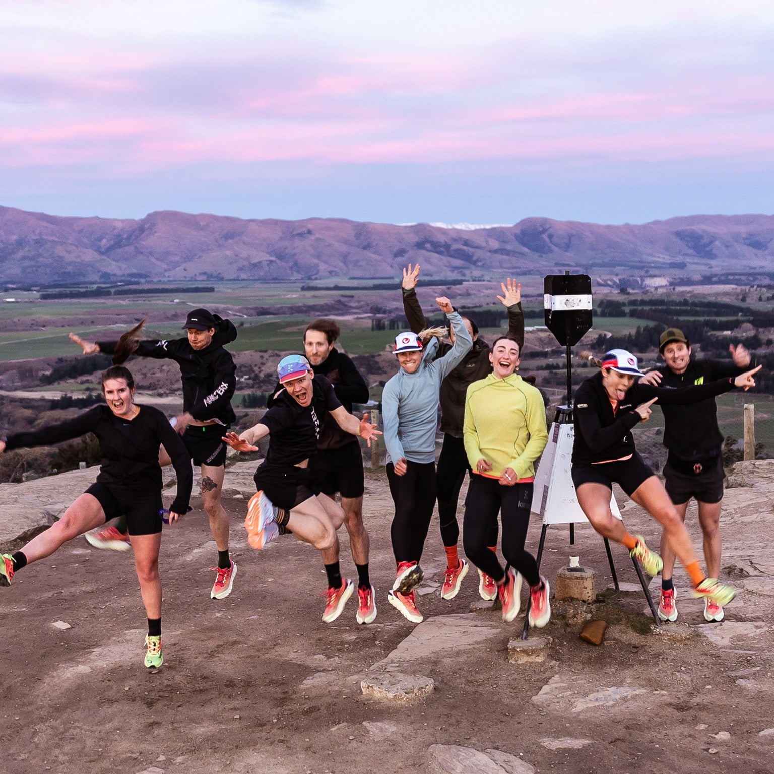 The Monday Coffee Run crew jumping for joy at the top of Mt Iron at sunrise, with Wānaka's mountains behind