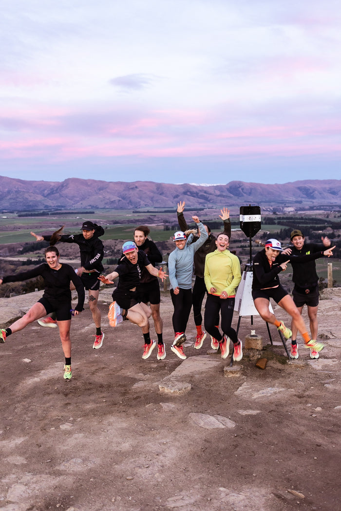 The Monday Coffee Run crew jumping for joy at the top of Mt Iron at sunrise, with Wānaka's mountains behind