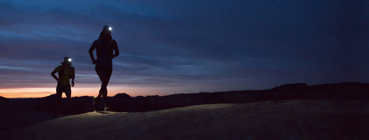 Two runners wearing Petzl headlamps on a ridge at dusk