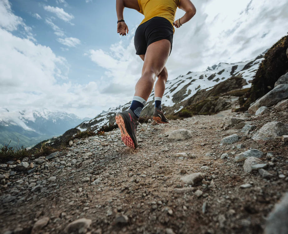 Trail runner on a rocky mountain path below snow-capped peaks